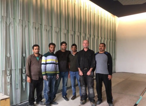 A member of our installations team with local contractors in front of the completed glass Majlis Wall for the Royal Palace.